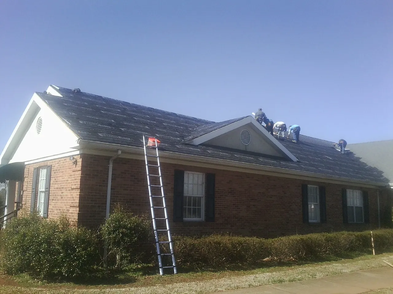 Crew tearing shingles off a brick ranch roof with a ladder set — Emergency Roof Repair work by our crew in Harveys Lake