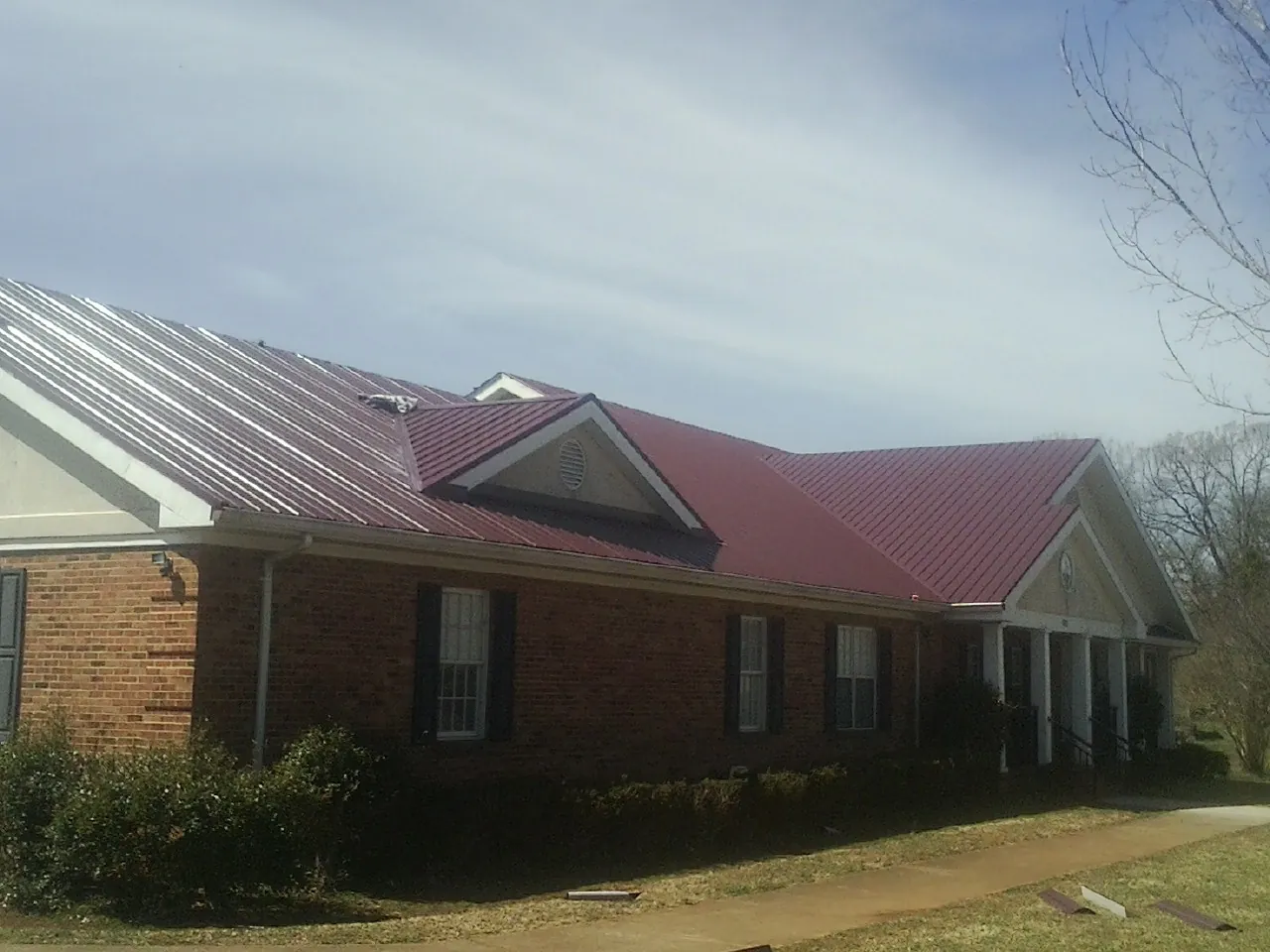 Red metal roof with gabled entries on a long brick building, from a Hail Damage Roof Repair job in Harveys Lake