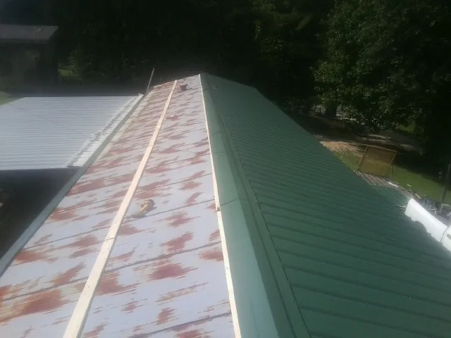 Old rusted panels beside newly installed green metal roofing — Wind Damage Roof Repair by Roofing Brothers in Harveys Lake