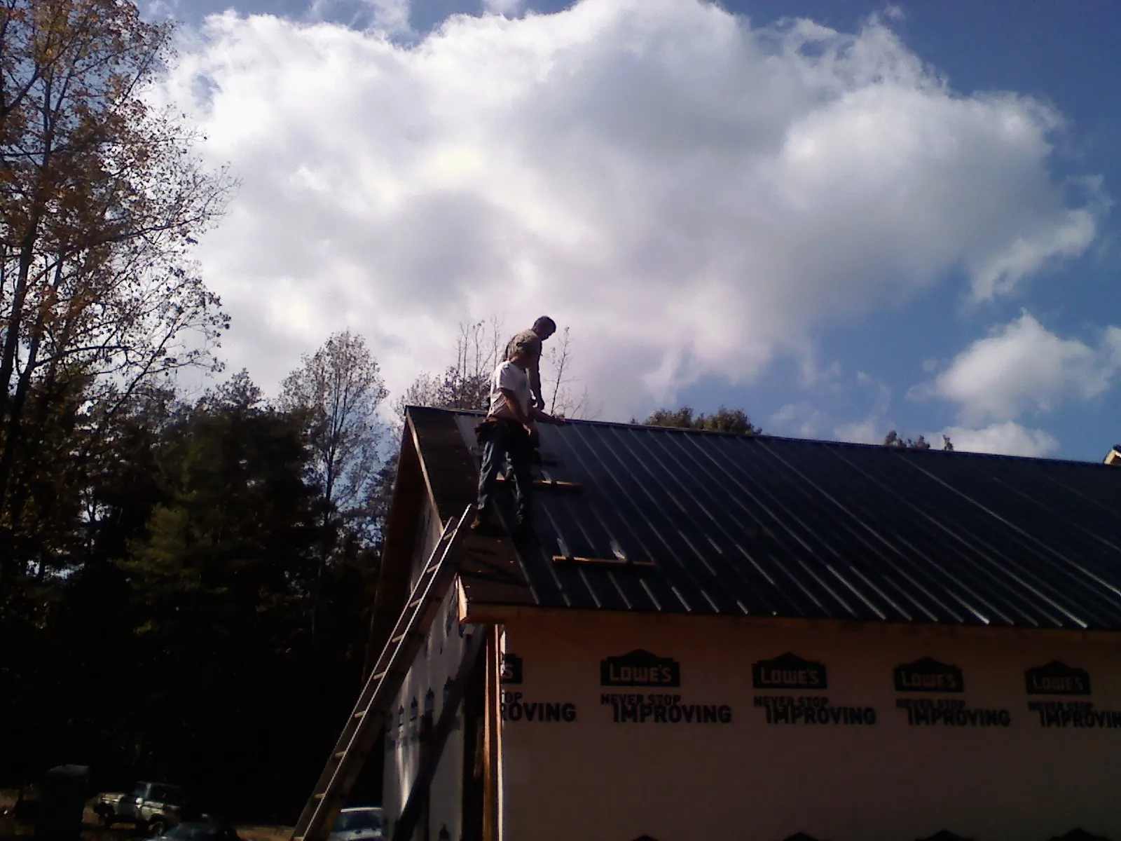 Roofer fastening dark metal panels high against a cloudy sky, from a Roof Inspection job in Harveys Lake