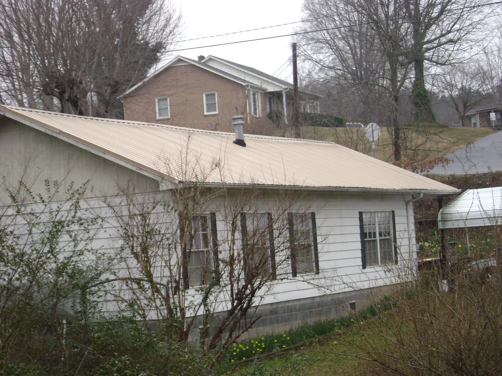 Tan metal roof on a white sided house set into a hillside — Commercial Roofing by Roofing Brothers in Harveys Lake